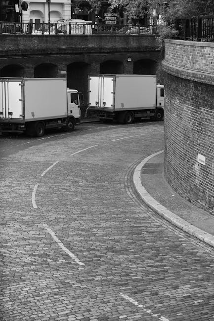 The image shows a house removal scene on Sloane Street, with a moving truck parked on the pavement adjacent to a multi-storey building with beige stone facades and several windows. Two movers, wearing